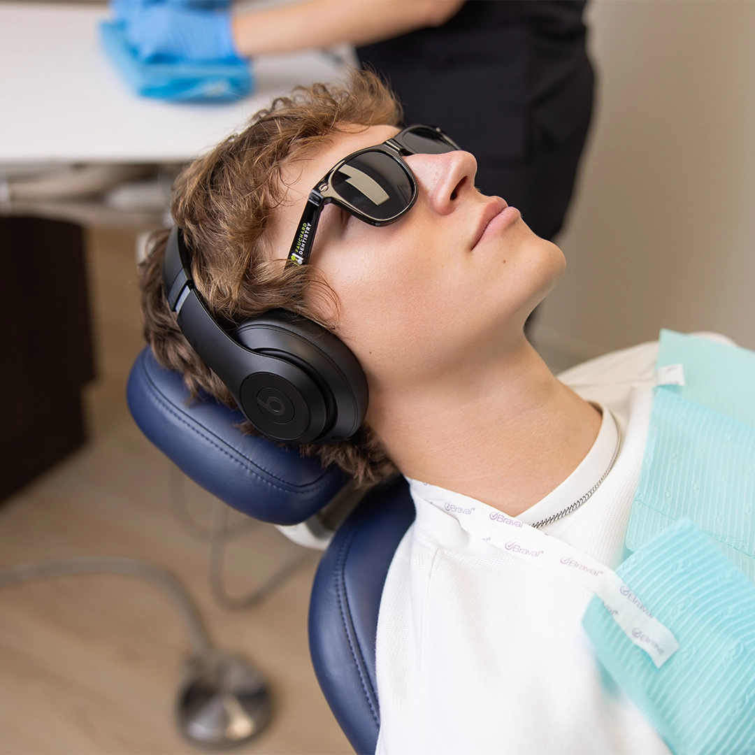 fauchard dentistry patient relaxing in dental chair with headphones and sunglasses